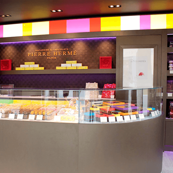 ntérieur d’une boutique Pierre Hermé avec vitrine de macarons et éclairage coloré au plafond.