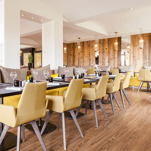 Salle de restaurant moderne avec chaises jaunes, tables dressées et éclairage suspendu chaleureux.